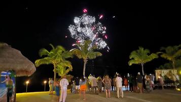 Reunión en la playa con gente mirando fuegos artificiales.