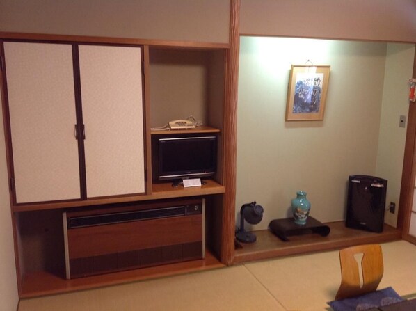 A traditional Japanese-style room with a sliding door, a television, a telephone, a framed picture on the wall, and a small table with a vase.