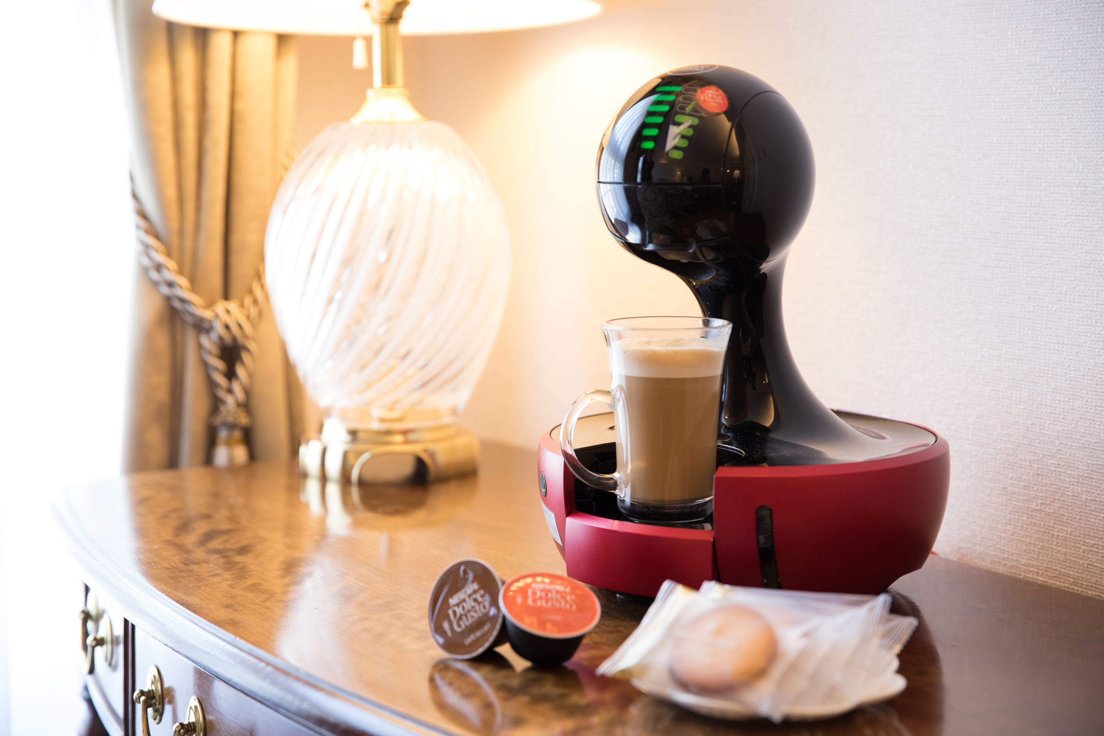A coffee machine with a cup of coffee, a tissue box, and a tissue on a wooden surface.