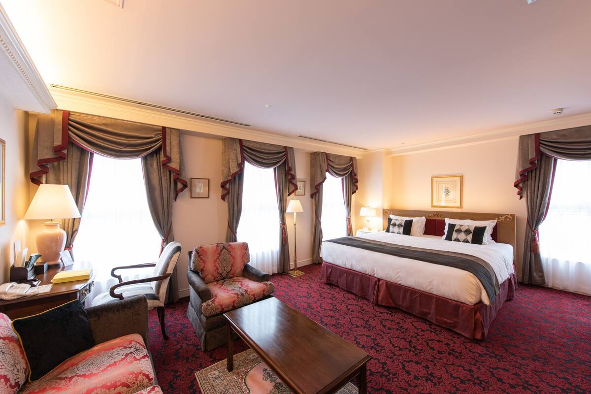 Ein Hotelzimmer mit einem großen Bett, einem Schreibtisch mit Lampe, einem Sessel und Teppichboden.