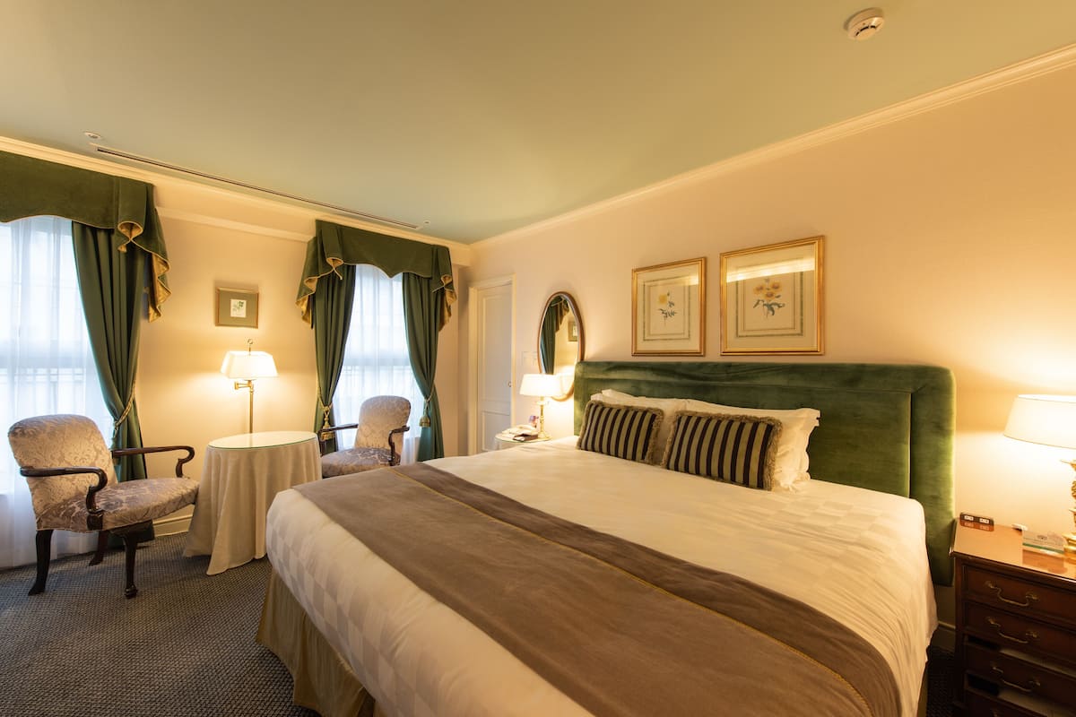 Ein Hotelzimmer mit einem großen Bett, zwei Nachttischen, einem Sessel und einem kleinen Tisch.