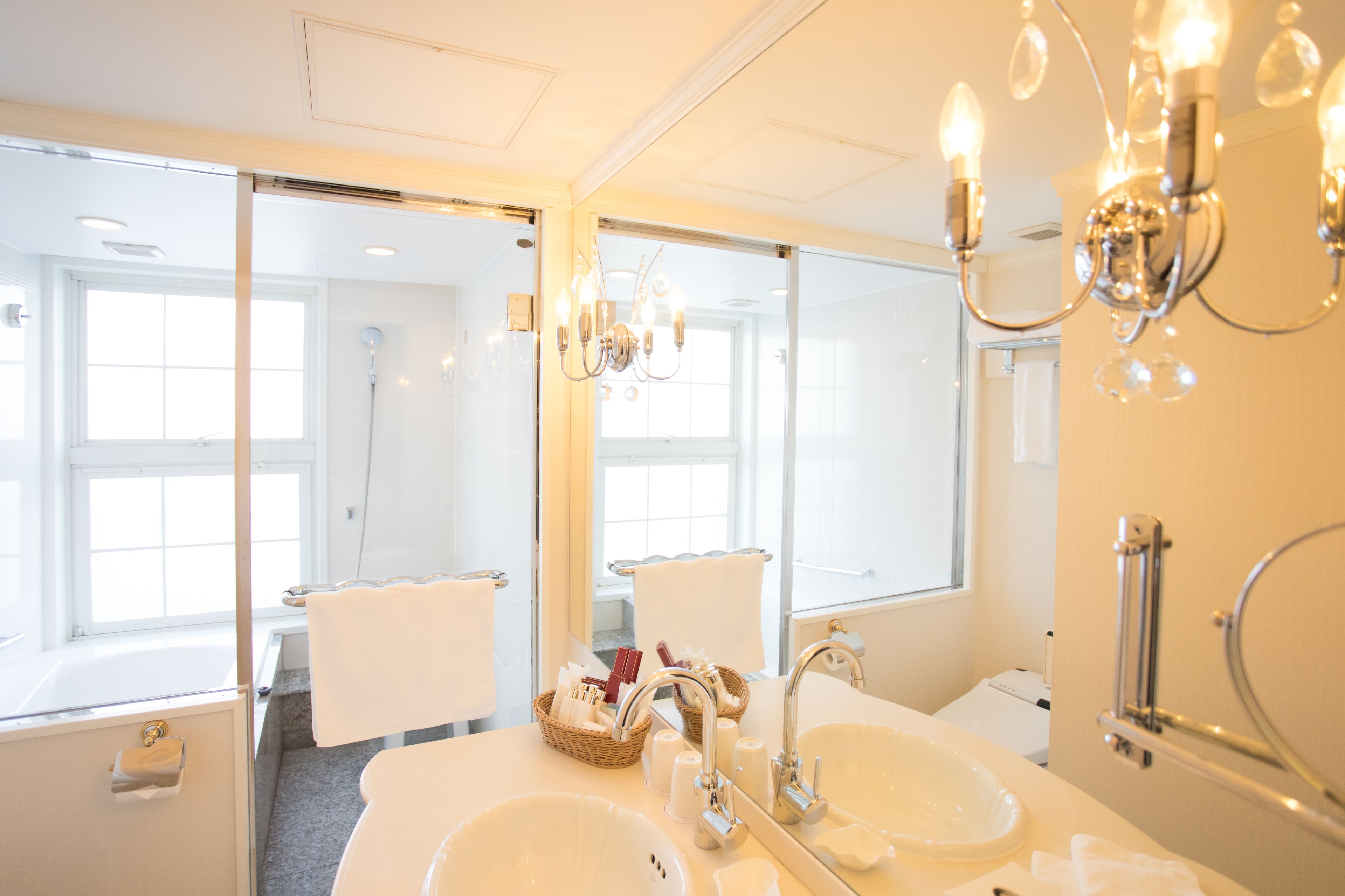 A bathroom with two sinks, a mirror, a chandelier, and a window.