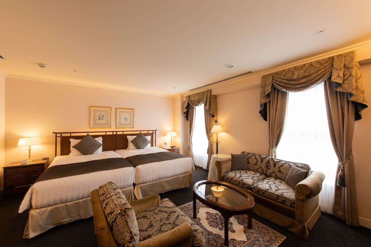 Ein Hotelzimmer mit einem Doppelbett, zwei Nachttischen mit Lampen, einem Sofa, einem Couchtisch und einem gemusterten Teppich.