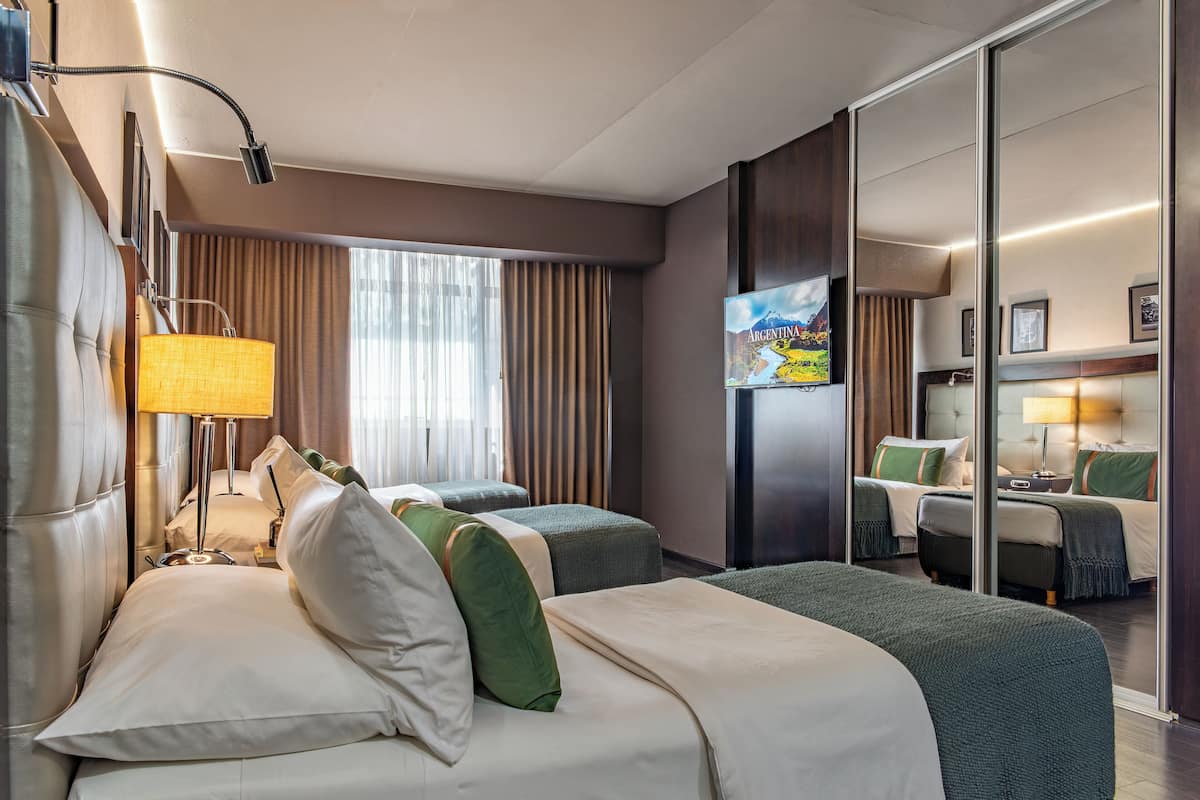 A hotel room with two beds, a large window with curtains, a flat-screen TV, and a mirror.