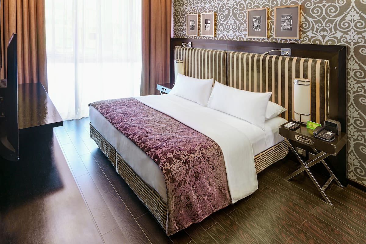 A hotel room with a large bed, a bedside table with a lamp, a TV, and framed pictures on the wall.