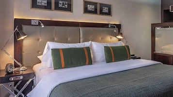 Habitación de hotel con una cama grande, dos lámparas de noche, una mesita de noche y cuadros en la pared.