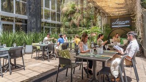 Un área de comedor al aire libre con mesas y sillas, rodeada de vegetación y un edificio con un letrero que dice "Lennox Hotels".