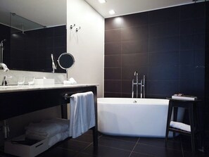 Un baño moderno con una bañera grande, un tocador con espejo y paredes de azulejos oscuros.