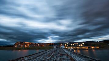 A wooden pier leading to a building with multiple windows and a flat roof, overlooking a body of water.