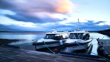 Two boats tied at a wooden dock with a calm body of water and a cloudy sky in the background.