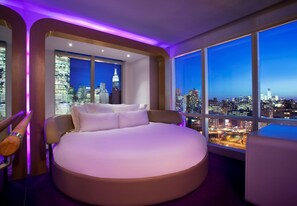 A modern bedroom with a large bed, a view of a cityscape, and purple ambient lighting. - YOTEL New York Times Square (New York)