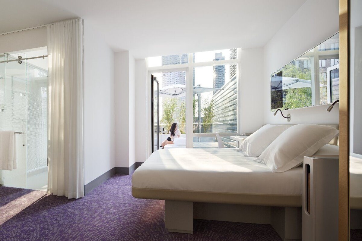 Una camera d'albergo con un letto, una TV, una doccia e vista sulla città.
