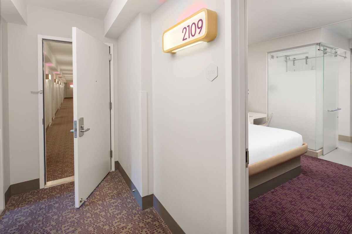 A hotel room with a bed, a shower, and a hallway leading to other rooms.