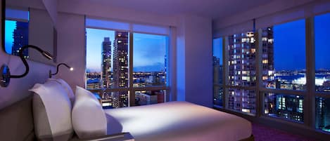 A modern bedroom with a bed, large windows, and a city view.