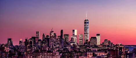 A city skyline at dusk with prominent skyscrapers, including a tall, illuminated building in the center.