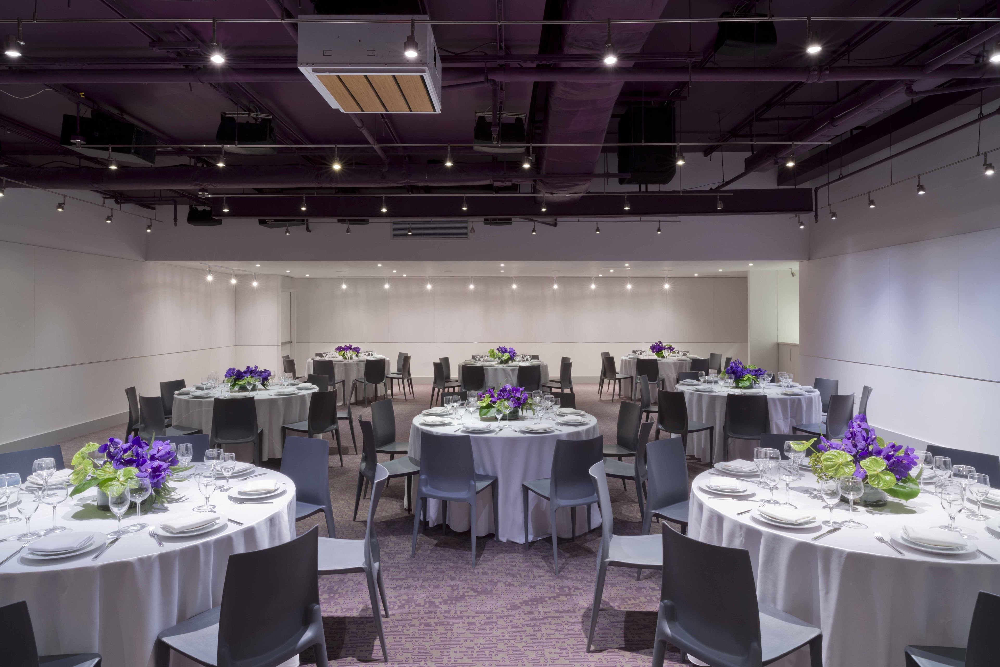 A conference room with multiple round tables, each set with white tablecloths, chairs, and floral centerpieces.