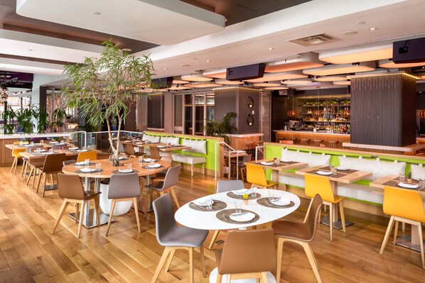 A modern restaurant with wooden flooring, round tables, and a variety of seating options. - YOTEL New York Times Square (New York)