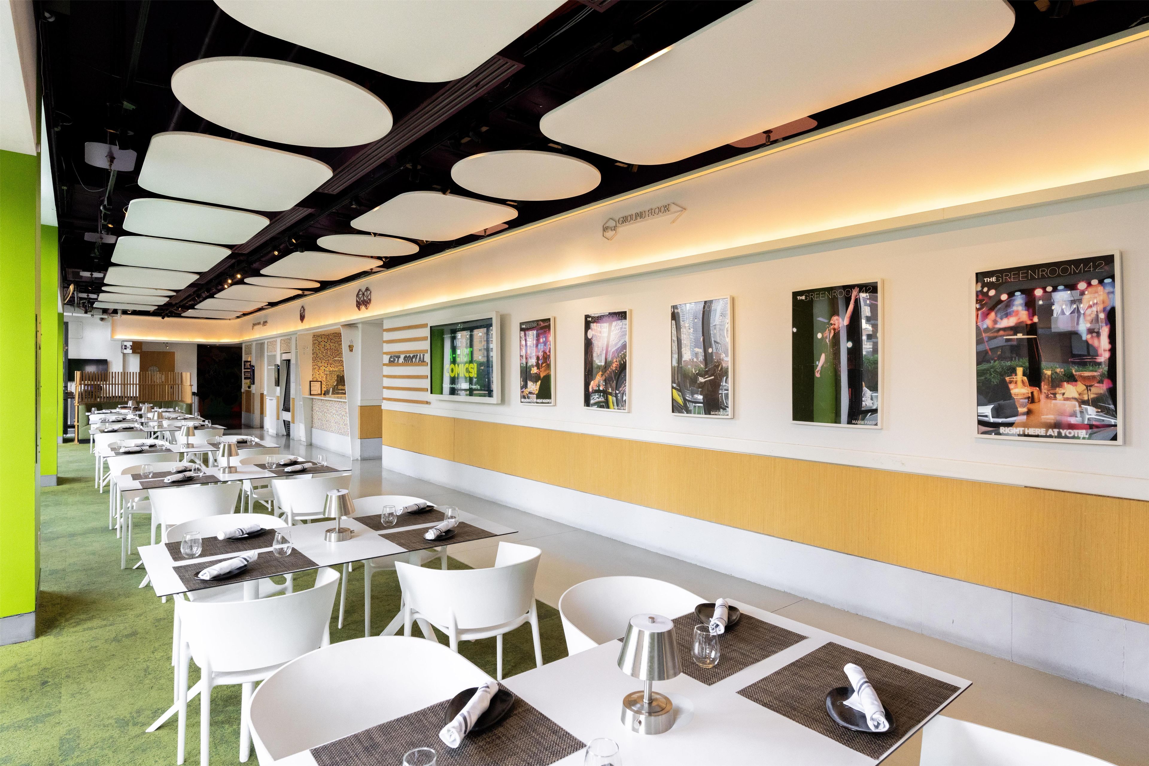 Un espace repas moderne avec des tables et des chaises blanches, un mur d’accent vert et des affiches encadrées accrochées au mur.