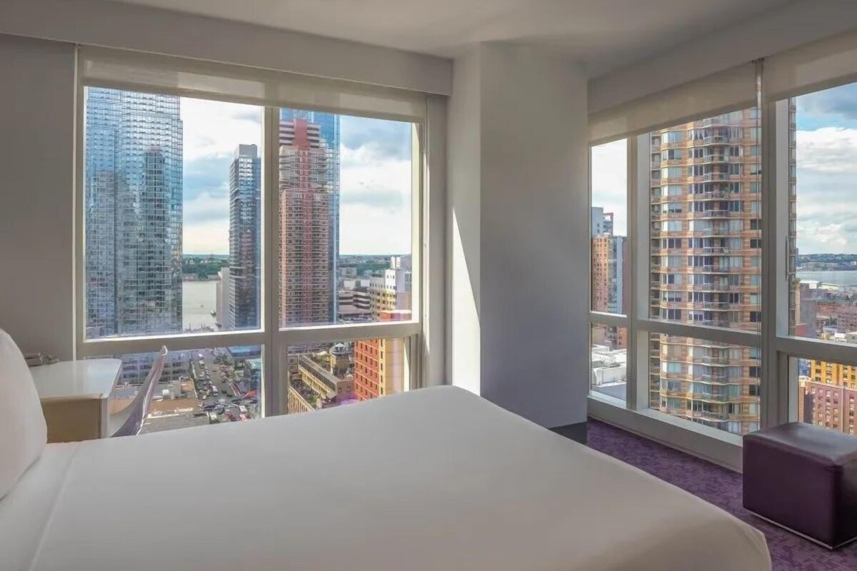Una camera d'albergo con un letto grande, due finestre e vista sugli edifici della città.