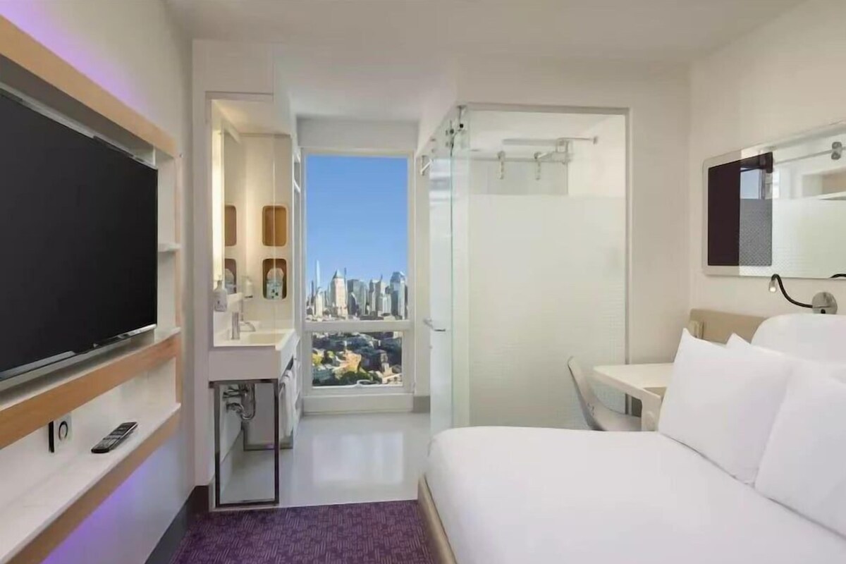 Una camera d'albergo con un letto, una TV, un bagno e una scrivania con vista sulla città.