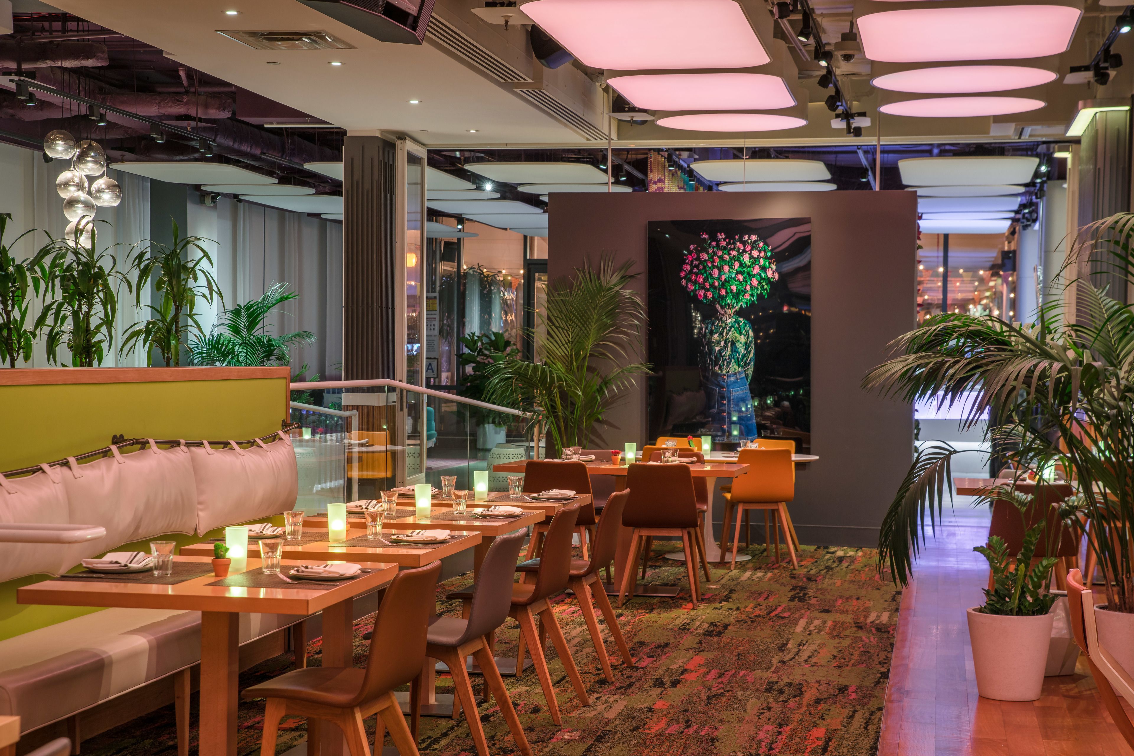Un restaurante moderno con mesas y sillas de madera, un banco tapizado de color verde y plantas en macetas.
