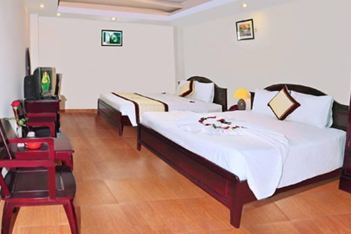 A hotel room with two beds, a wooden wardrobe, a desk with a chair, and a television.