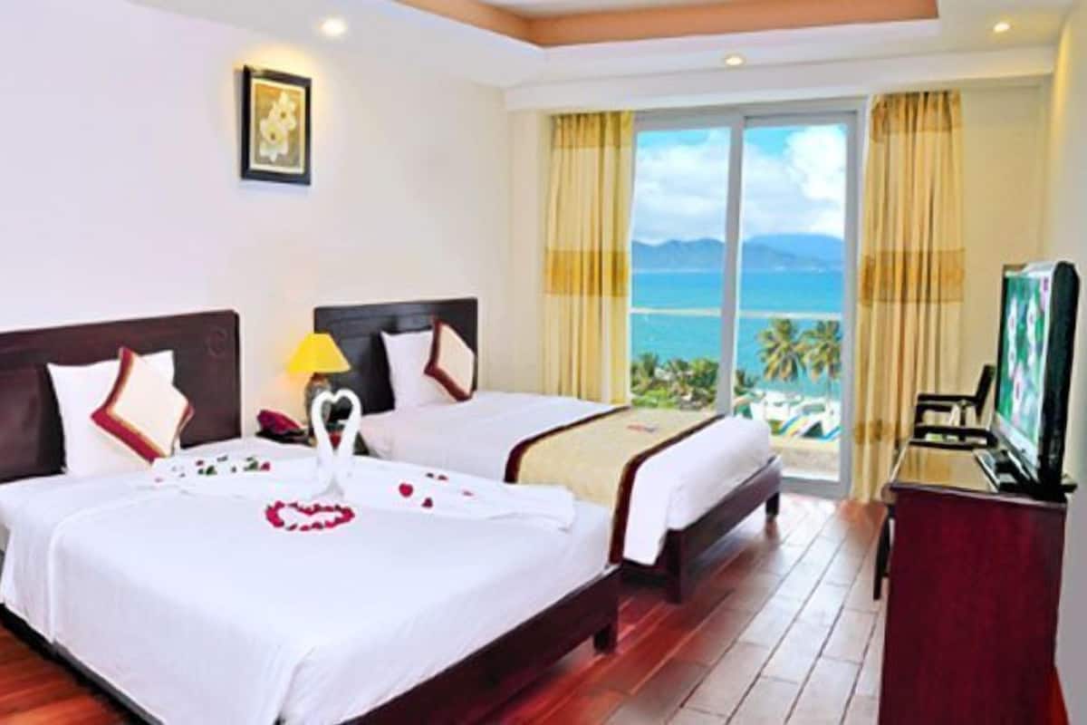 A hotel room with two beds, a desk, a chair, and a TV.