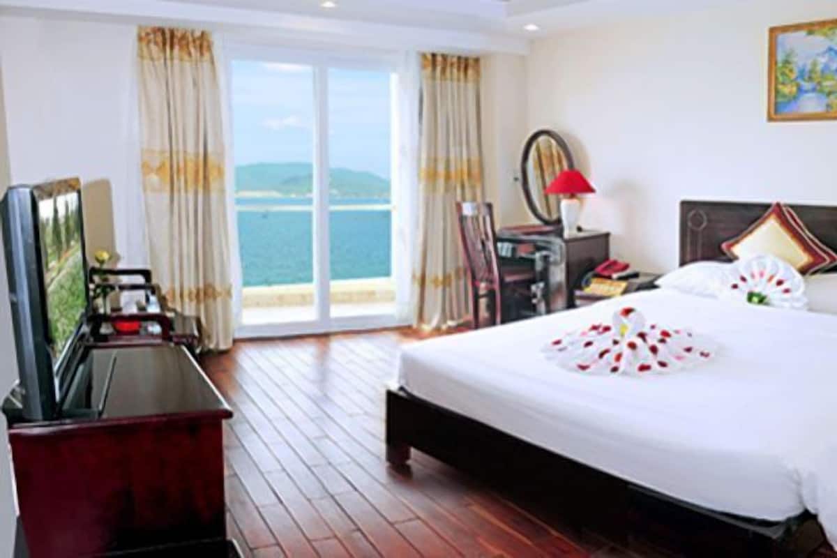 A hotel room with a large bed, a desk, and a view of the sea.