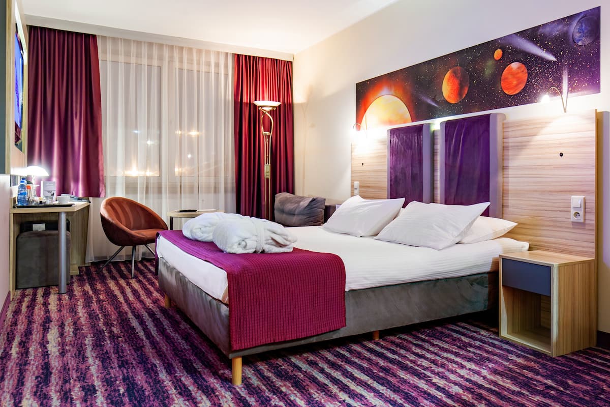 Habitación de hotel con cama, escritorio, silla, mesita de noche y un cuadro grande en la pared con planetas.