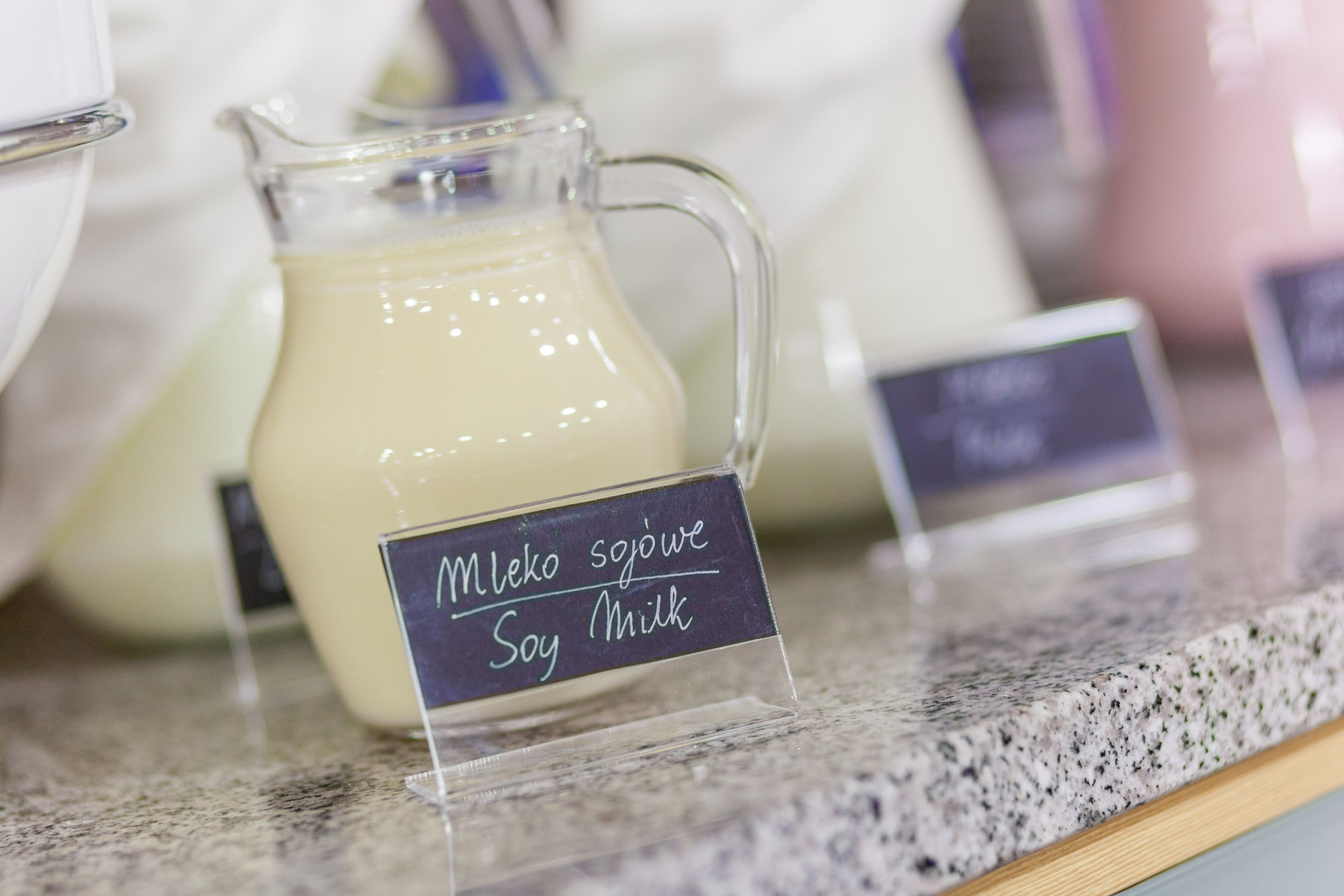 A glass pitcher of soy milk labeled "Mleko sojowe Soy Milk" on a granite countertop.