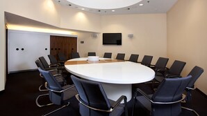 Une salle de conférence équipée d’une table ronde, de chaises noires, d’un téléviseur à écran plat et d’un éclairage encastré au plafond.