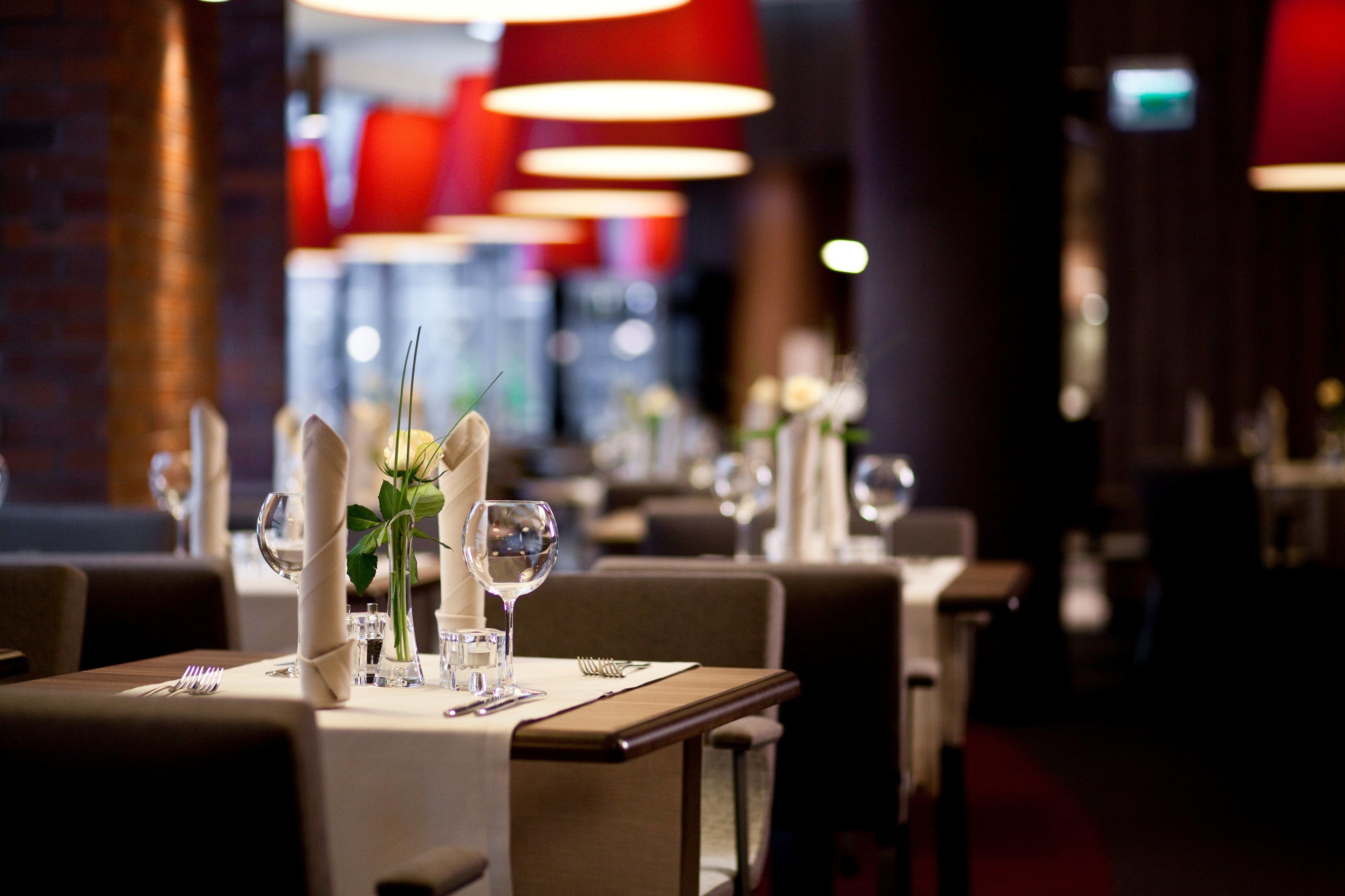 A restaurant with tables set for dining, featuring white tablecloths, clear glassware, and a vase with a single flower.