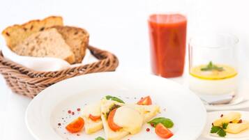 Une assiette de nourriture comprenant du pain, des tomates et un verre d’une boisson rouge.