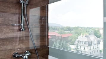 A modern bathroom with a glass shower enclosure, a wooden panel wall, and a view of a cityscape.