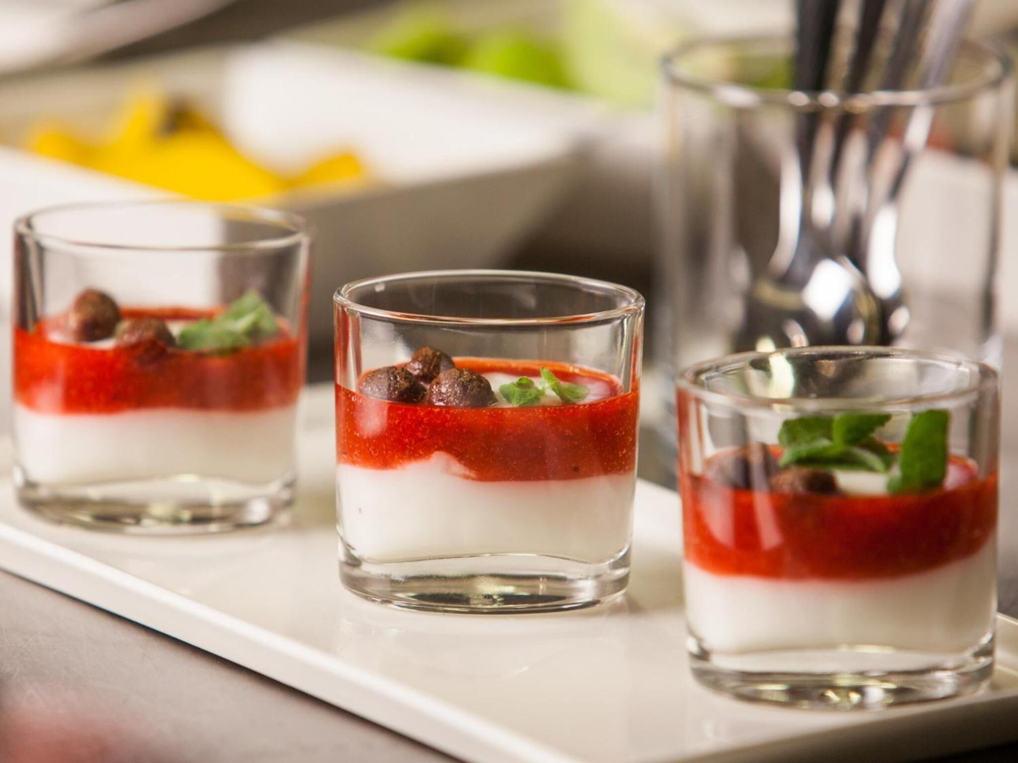 Three glasses of layered dessert with a red topping and mint garnish.
