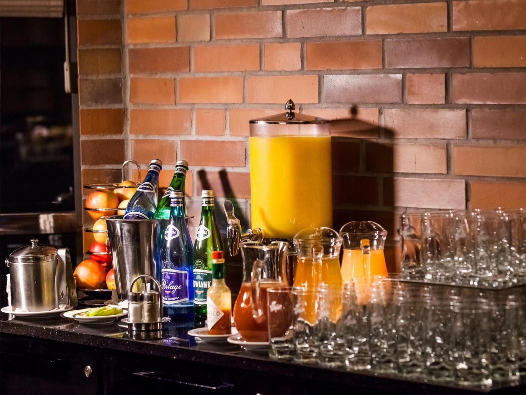 A bar area with various bottles, glasses, and a large yellow container, likely a punch bowl, against a brick wall.