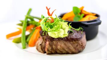 A steak with a garnish of green sauce and vegetables on a white plate.