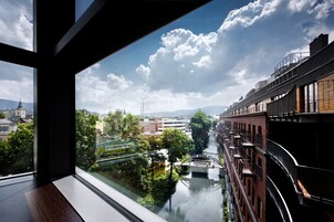 Vista desde una ventana sobre un río con un puente, edificios y vegetación.