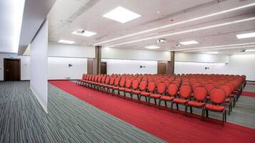 A conference room with rows of red chairs, a red carpet, and white walls.