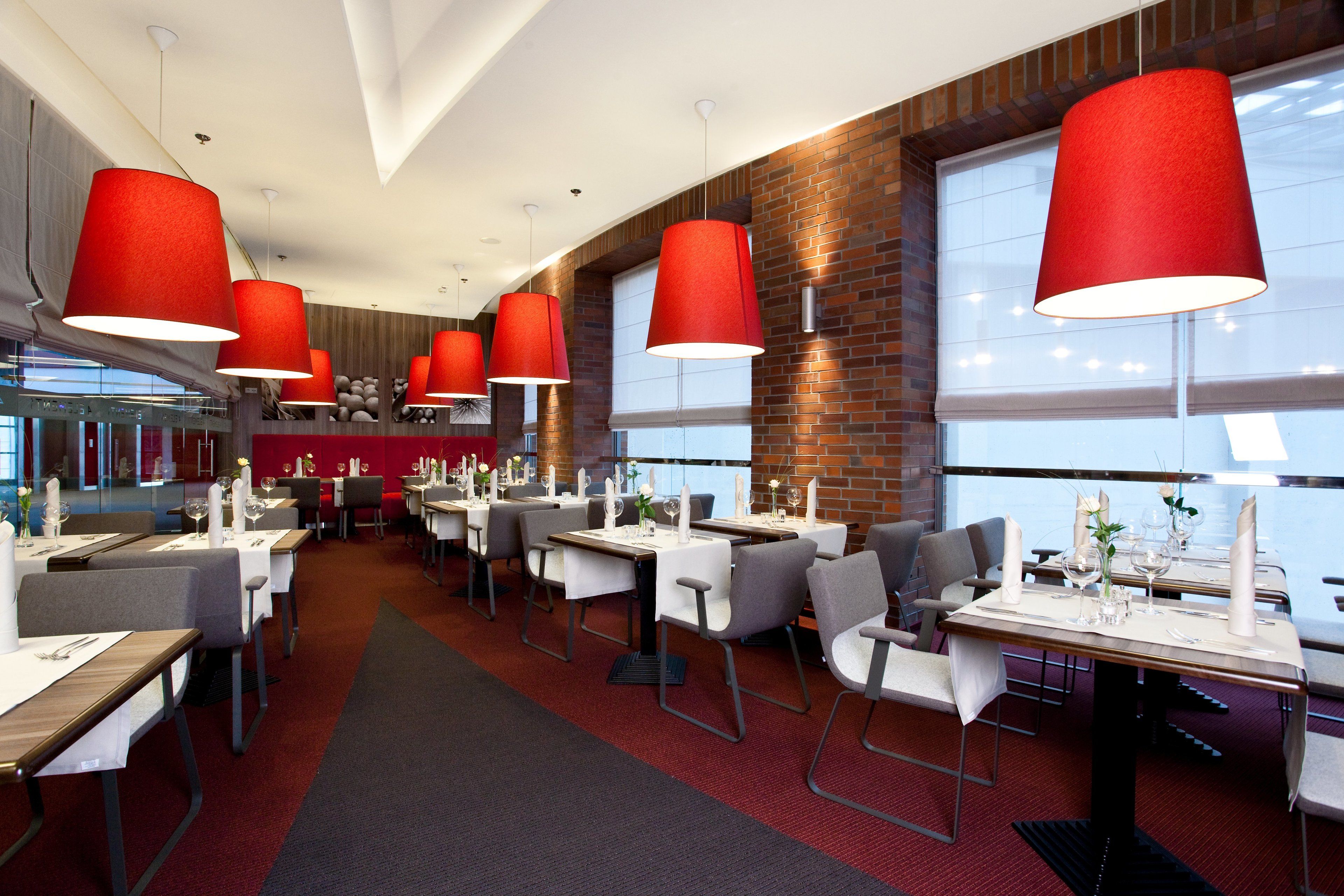 A modern restaurant with red pendant lights, white tablecloths, and grey chairs.