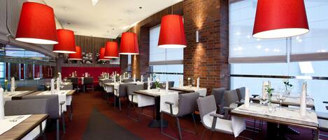 A modern restaurant with red pendant lights, white tablecloths, and grey chairs.