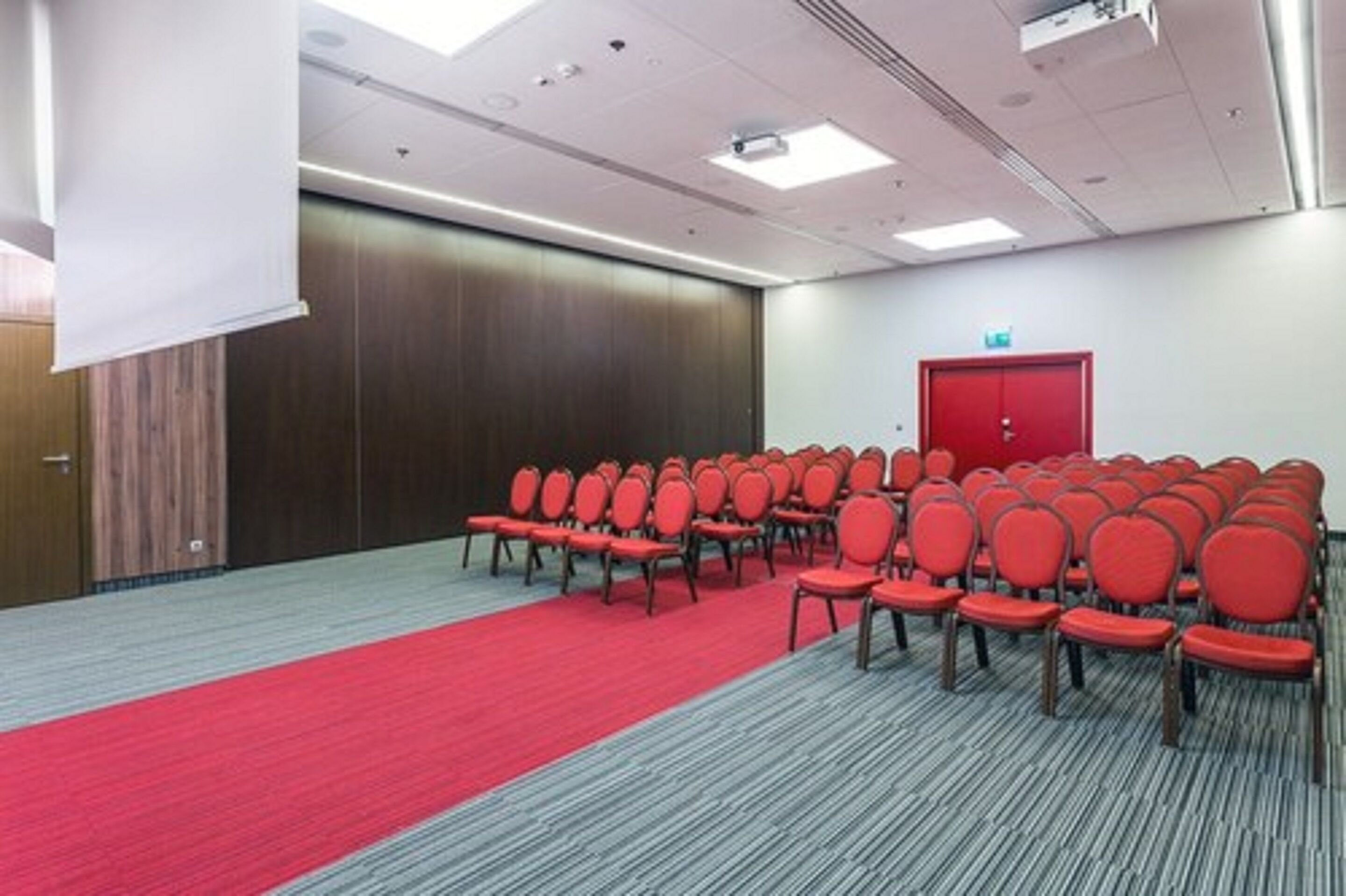 Un salón de conferencias con hileras de sillas rojas, una alfombra roja y un revestimiento de pared de madera.