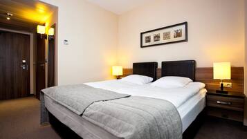 A hotel room with a large bed, two bedside tables with lamps, a framed picture on the wall, and a wooden door.
