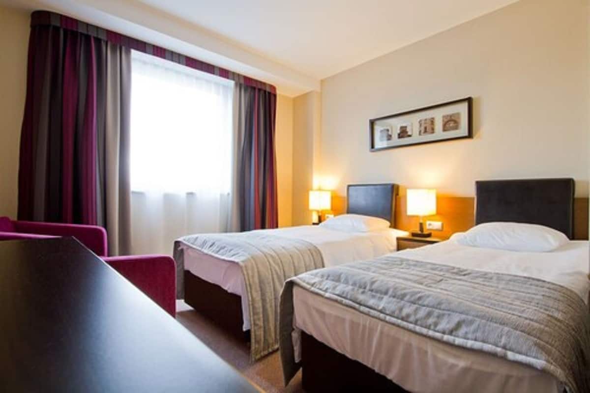 A hotel room with two beds, a desk, a chair, and a window with curtains.