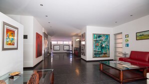Un hall d’entrée moderne avec une table basse en verre, un canapé rouge et diverses œuvres d’art accrochées aux murs.
