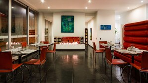 Un restaurant moderne doté d’un foyer central, de sièges rouges et d’œuvres d’art contemporaines accrochées aux murs.