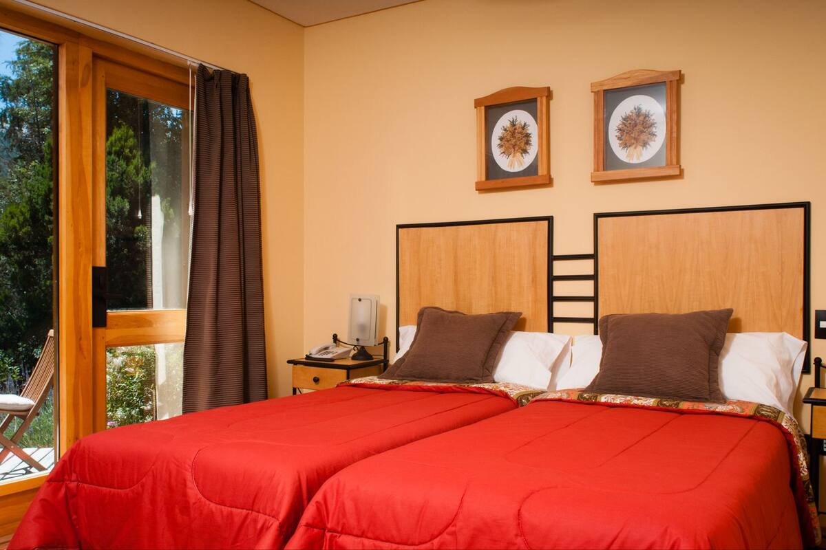 Ein Doppelbett mit roter Bettwäsche, ein Nachttisch mit Lampe und zwei gerahmte Bilder an der Wand.