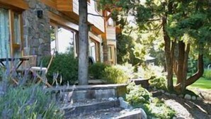 Eine rustikale Holzhütte mit Natursteinfassade, Holzbalken und einem Garten mit verschiedenen Pflanzen und einer Bank.