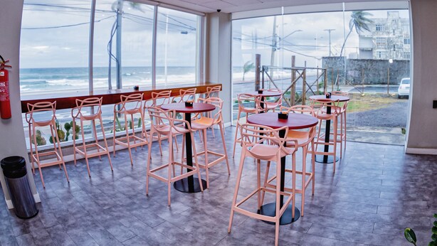 A restaurant with outdoor seating, large windows overlooking the ocean, and a view of the beach and palm trees. - B Hotel (Salvador)