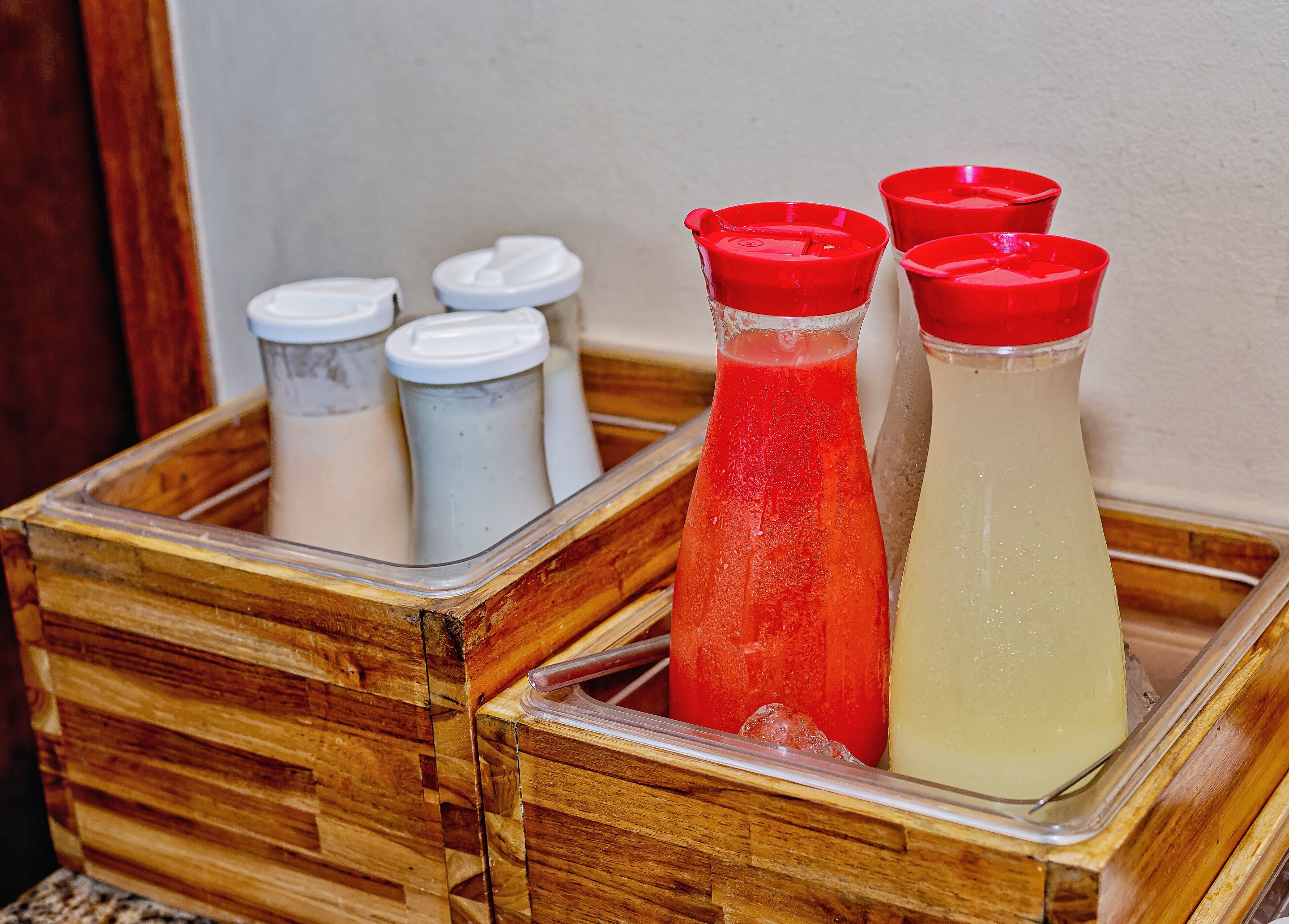 Una caja de madera con varias botellas que tienen tapones rojos y blancos, presumiblemente con bebidas.